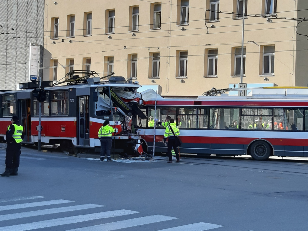 Rote und weiße Tram auf der Straße mit ein paar Menschen in der Nähe und einem Gebäude im Hintergrund.