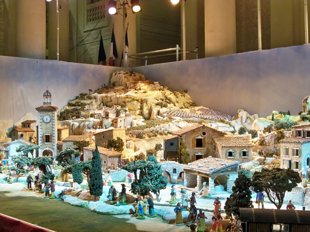 Ein detailliertes Miniatur-Weihnachtskrippen-Diorama in einem Museum, mit Figuren, Strukturen und beleuchteten Elementen.